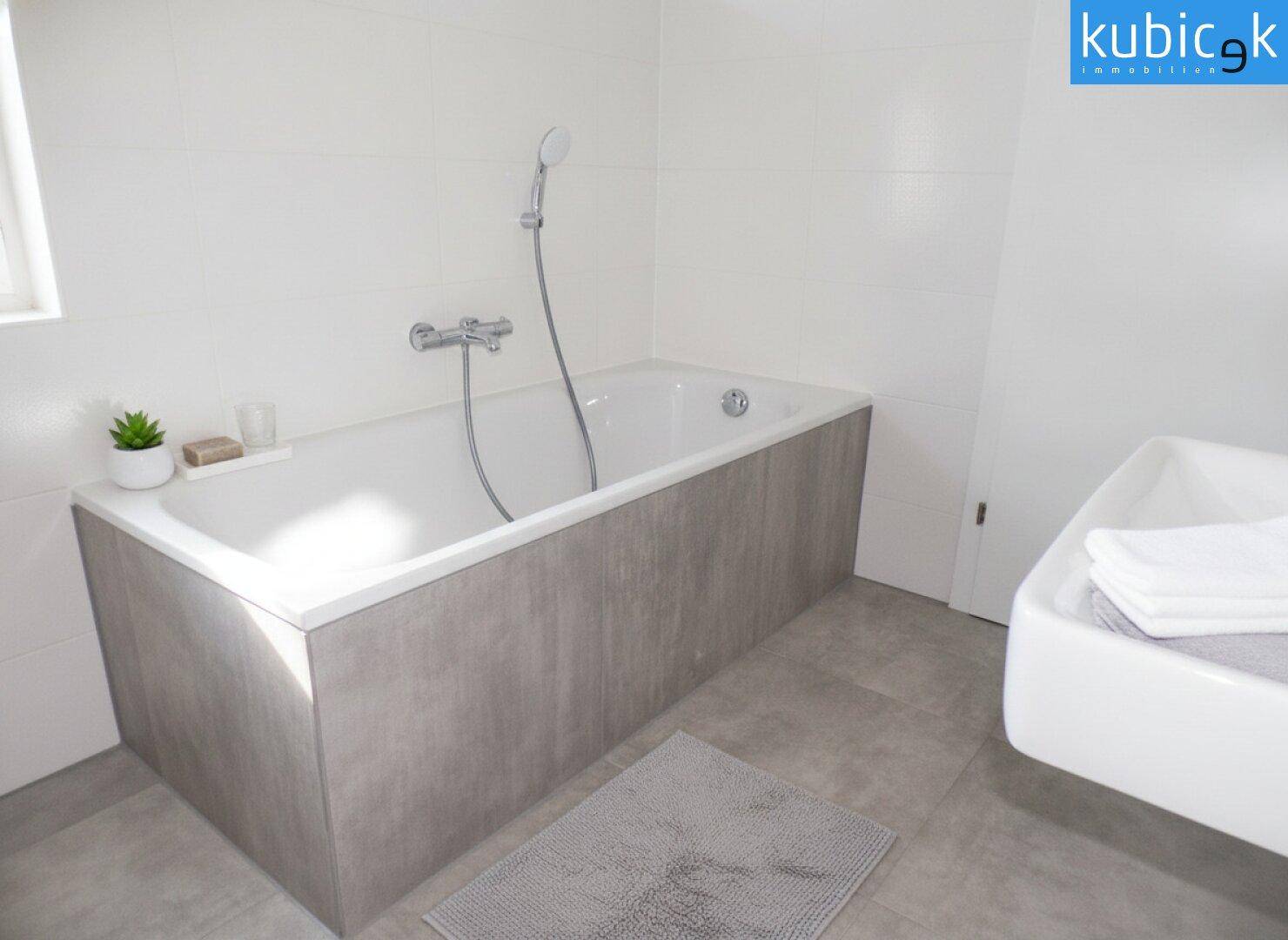 Modernes Badezimmer mit Badewanne, grauen Fliesen und weißer Wandverkleidung.
