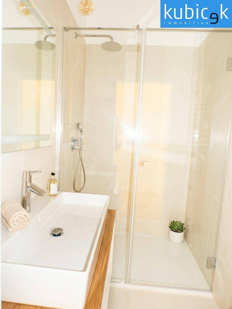 Modernes Badezimmer mit begehbarer Dusche, weißem Waschbecken und hellen Fliesen.