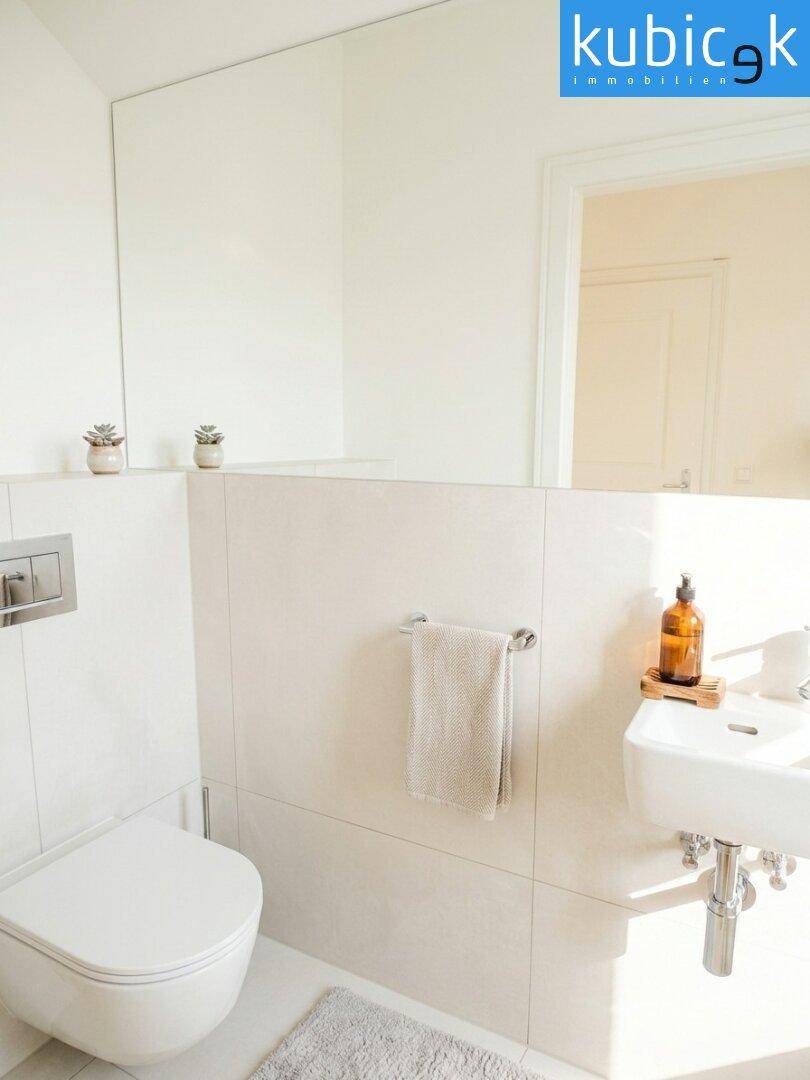 Modernes Gäste-WC mit wandhängender Toilette, kleinem Waschbecken und großem Spiegel.