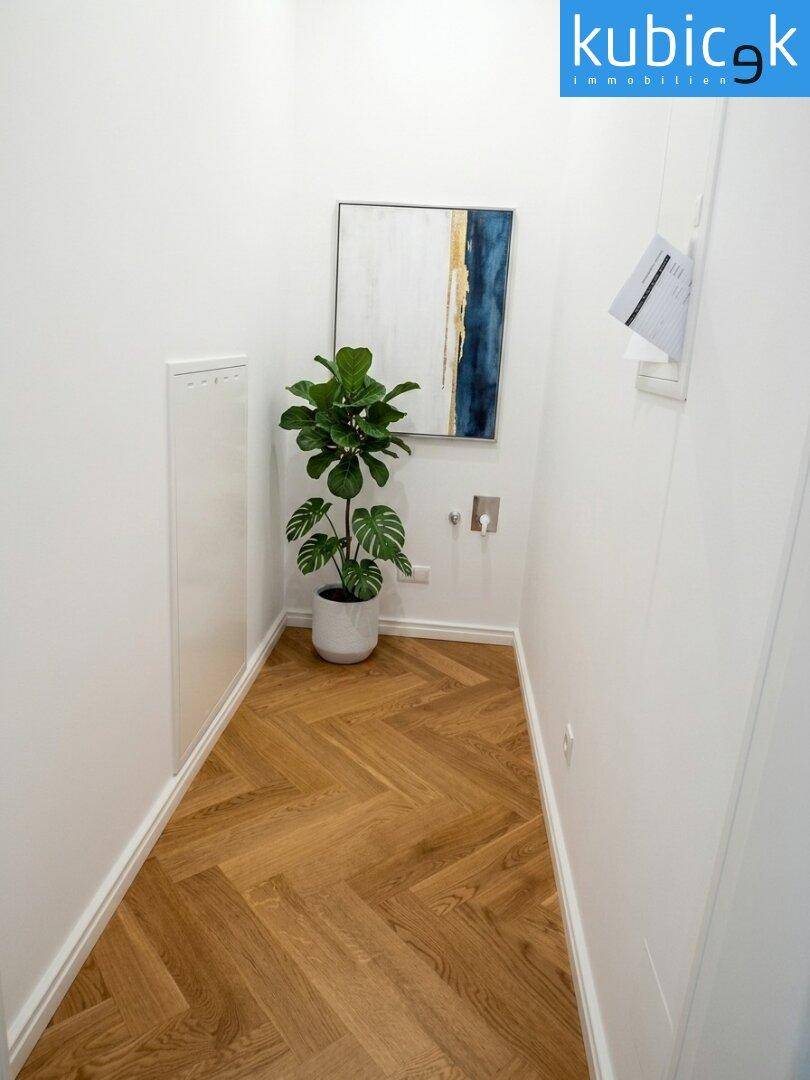 Schmaler Raum mit Fischgrätparkett, weiß gestrichenen Wänden und moderner Kunst.