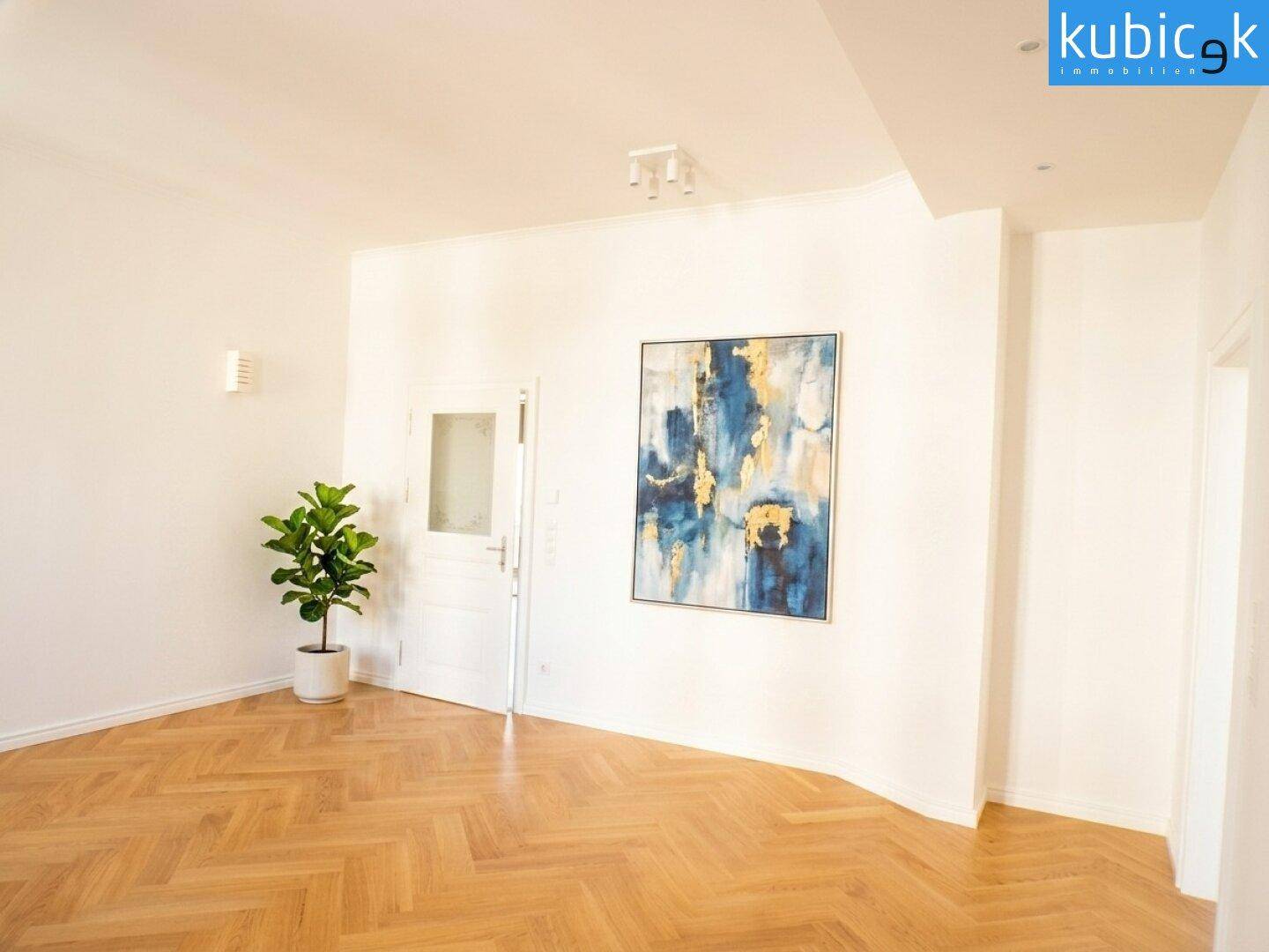 Lichtdurchfluteter Raum mit Fischgrätparkett und einer eleganten Eingangstür.