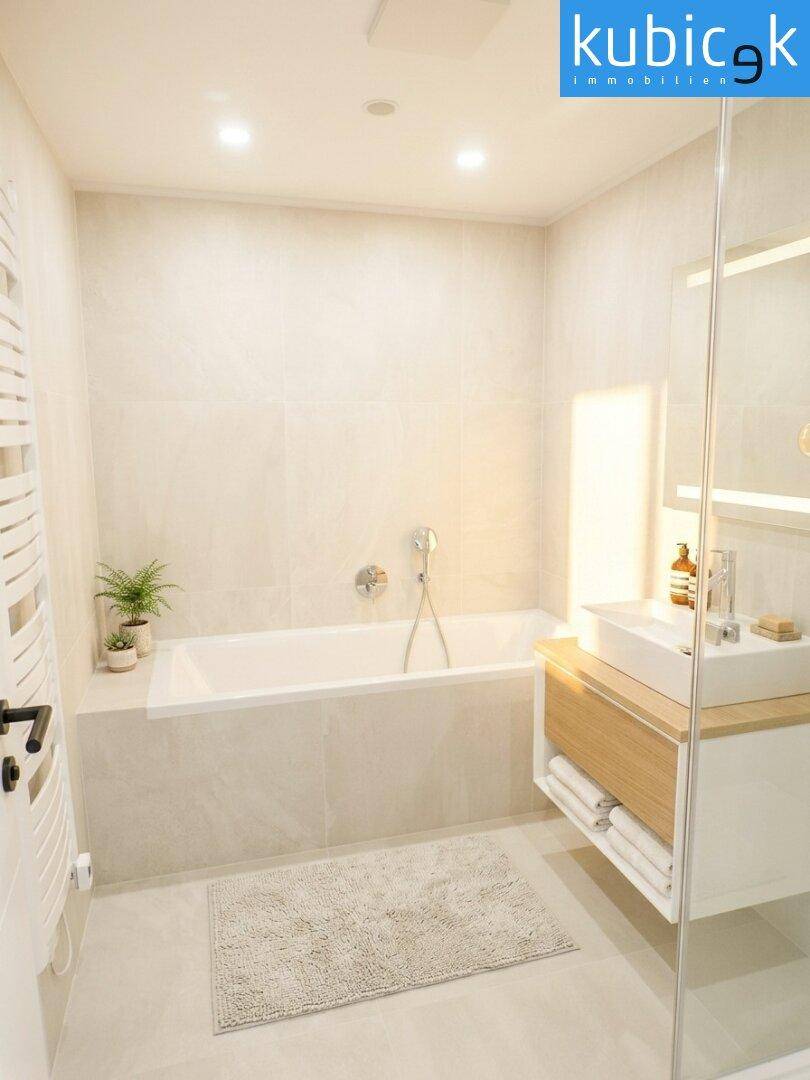 Modernes Badezimmer mit Badewanne, Einzelwaschbecken und hellen Fliesen, ausgestattet mit Handtuchheizkörper.