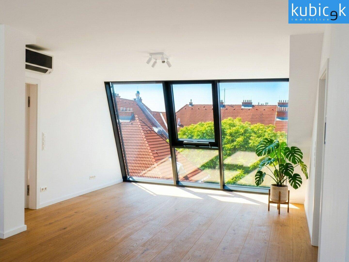 Lichtdurchfluteter Raum im Dachgeschoss mit schrägen Fenstern, Holzboden und Klimaanlage.