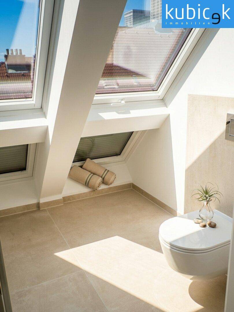 Modernes Badezimmer im Dachgeschoss mit WC, Fliesenboden und hellen Dachfenstern.