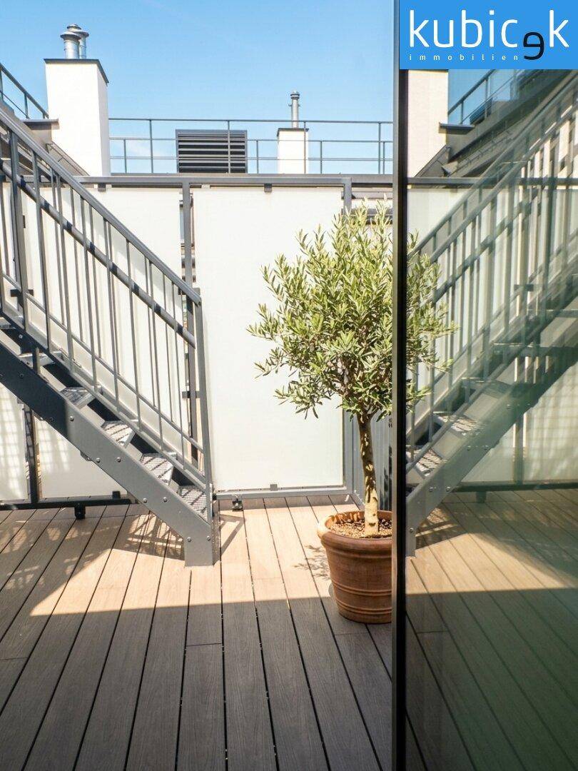 Dachterrasse mit Holzboden, Metallgeländer und mediterranen Pflanzen in Töpfen.