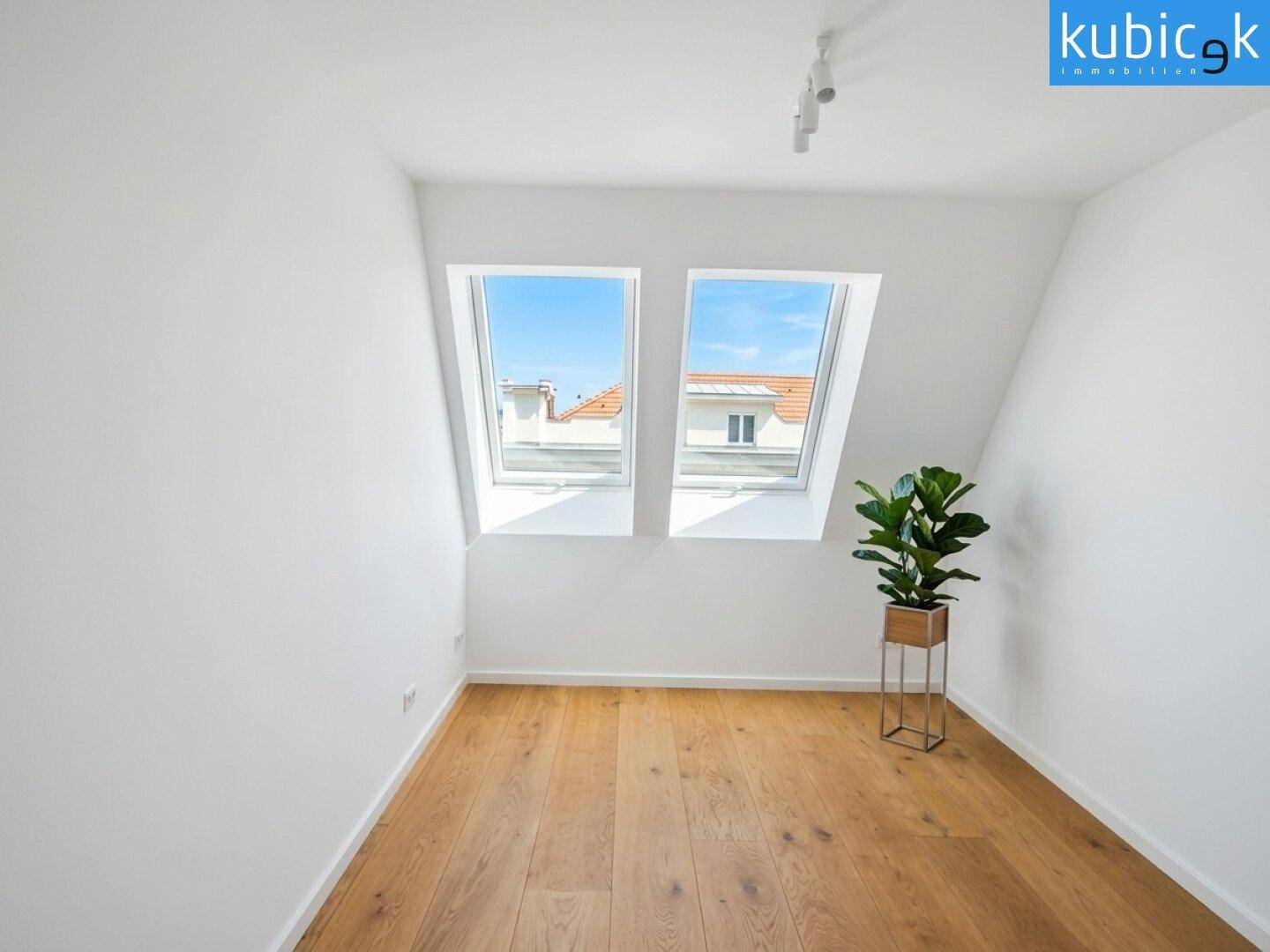 Helles Schlafzimmer im Dachgeschoss mit Holzboden, zwei Dachfenstern und schrägen Wänden.