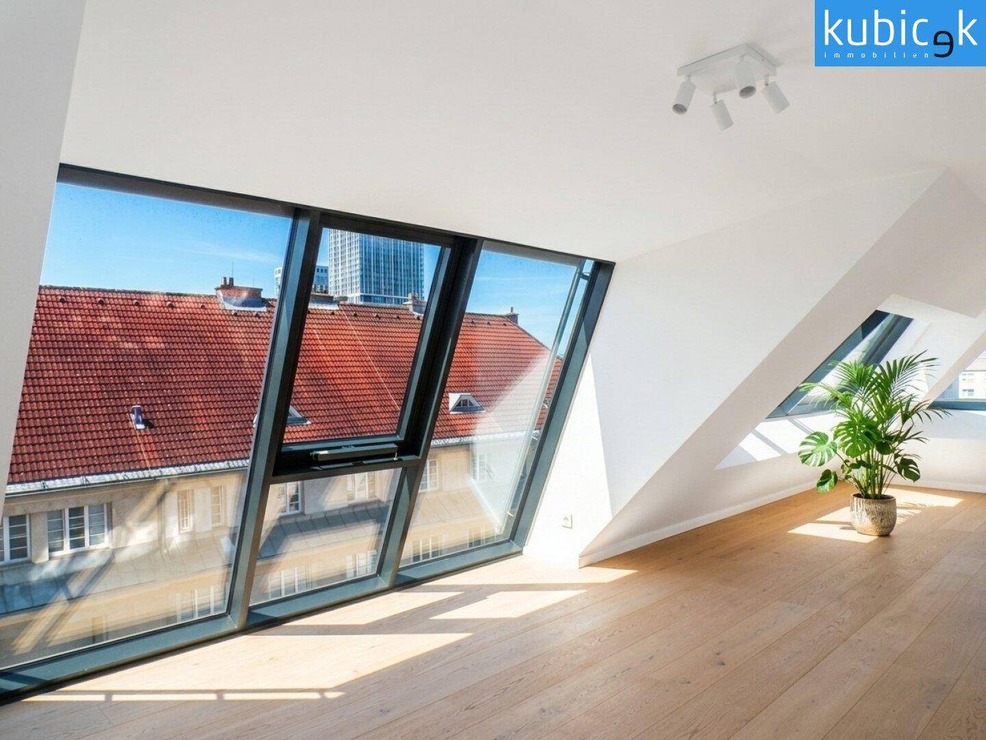 Heller Dachgeschossraum mit großen Fenstern, Holzboden und weitem Blick über die Dächer der Stadt.