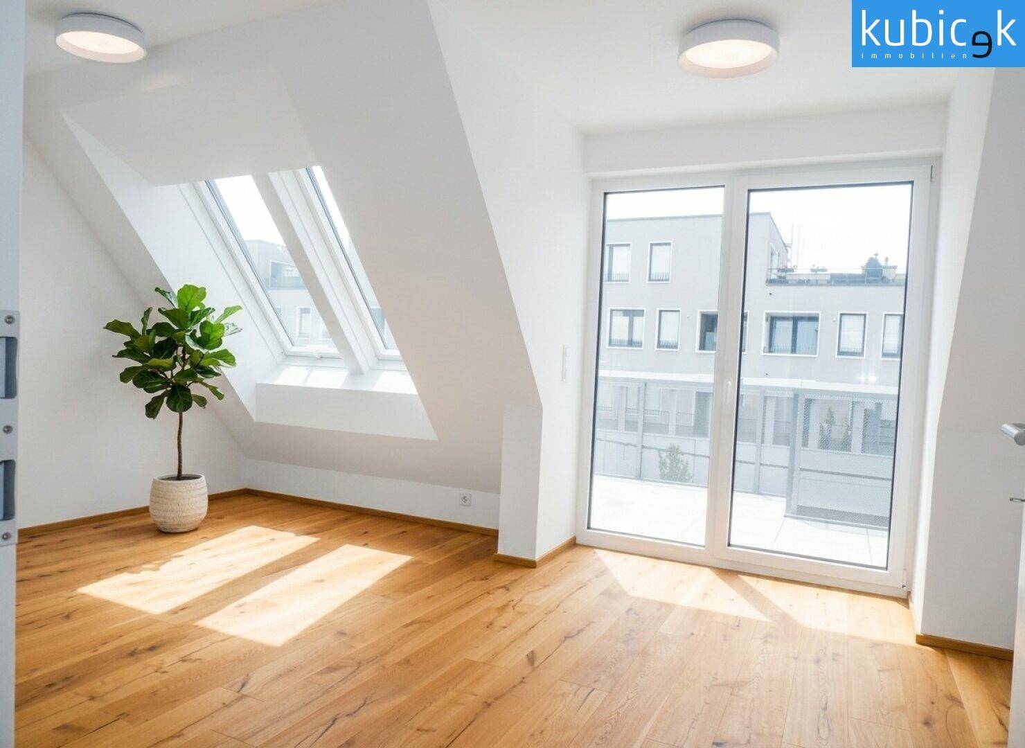 Helles Dachgeschosszimmer mit Holzboden, großen Fenstern und Zugang zu einem Balkon.