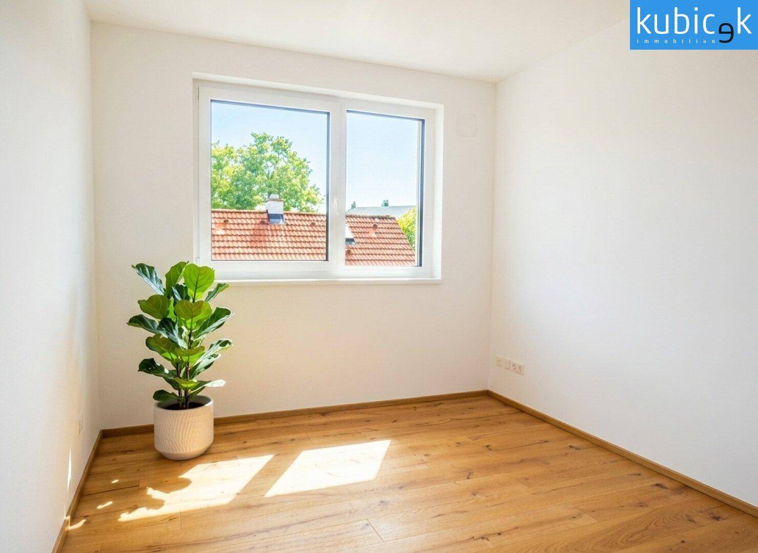 Freundliches Zimmer mit Holzboden und Blick auf die umliegenden Dächer und Bäume.