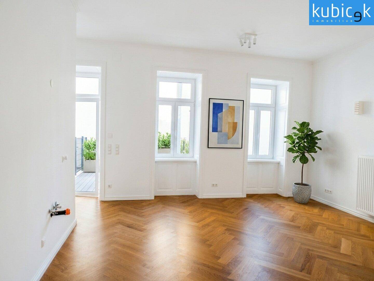 Helles Zimmer mit elegantem Fischgrätparkett, großen Fenstern und einem Heizkörper unter dem Fenster.