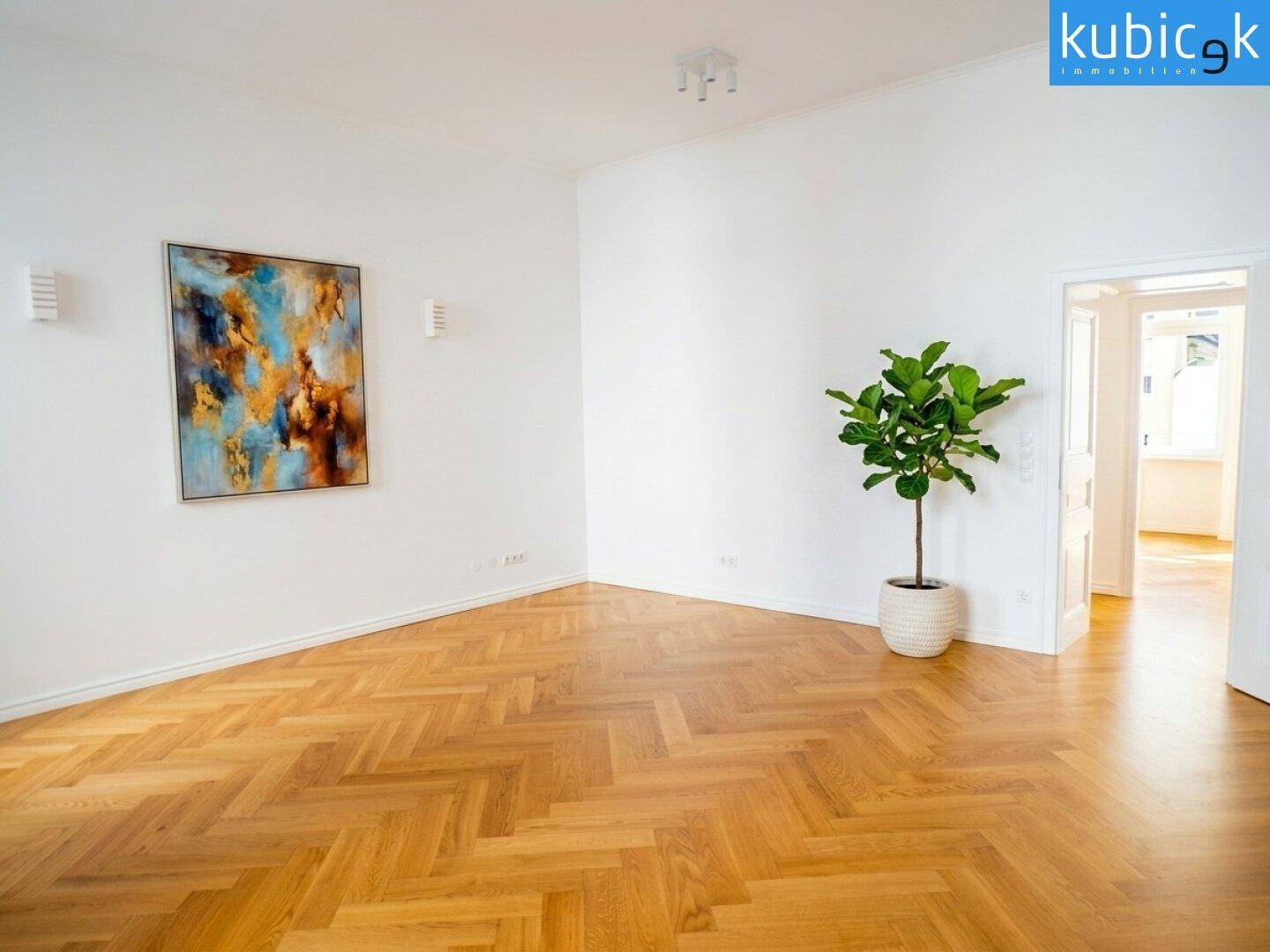 Leeres Zimmer mit Fischgrätparkett, weißen Wänden und einem modernen Kunstwerk als Blickfang.