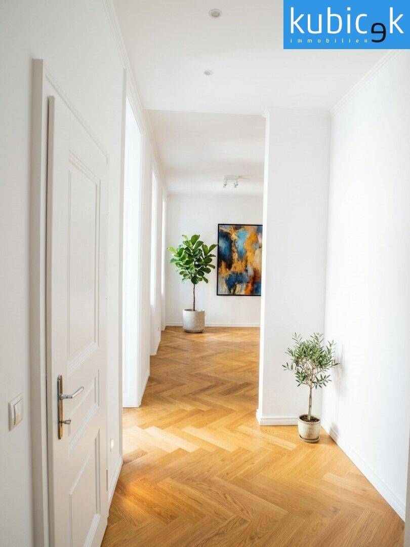Langer, heller Flur mit Fischgrätparkett und weißen Wänden, der zu weiteren Räumen führt.