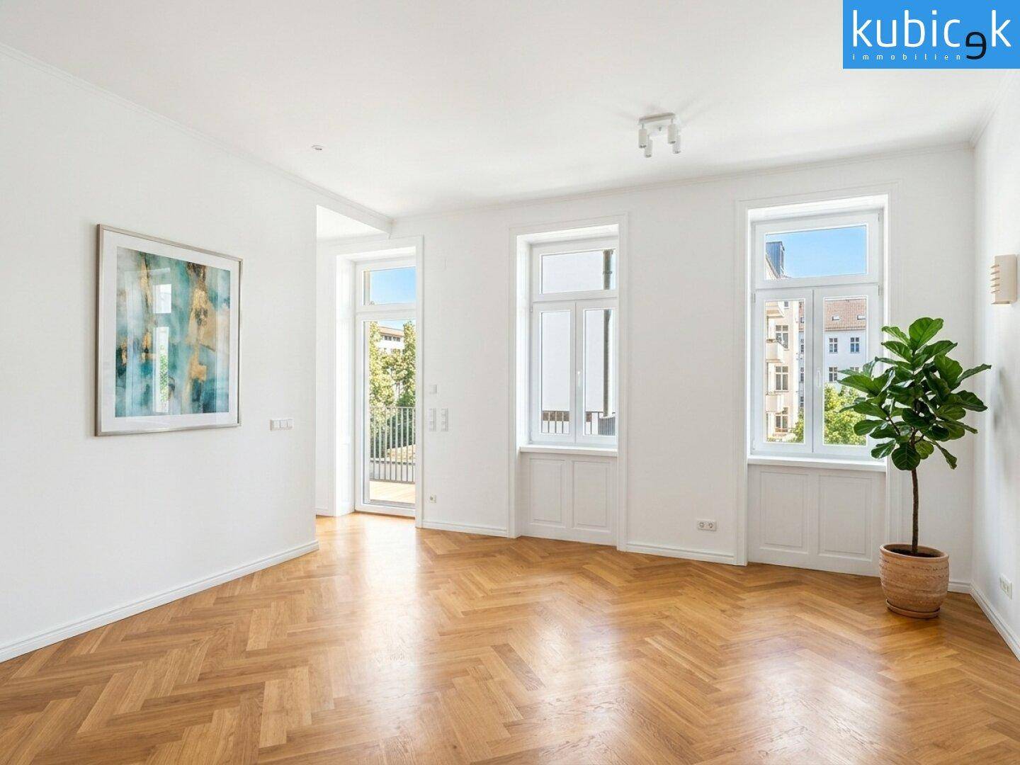 Helles Wohnzimmer mit Fischgrätparkett, hohen Fenstern und Zugang zu einem Balkon.