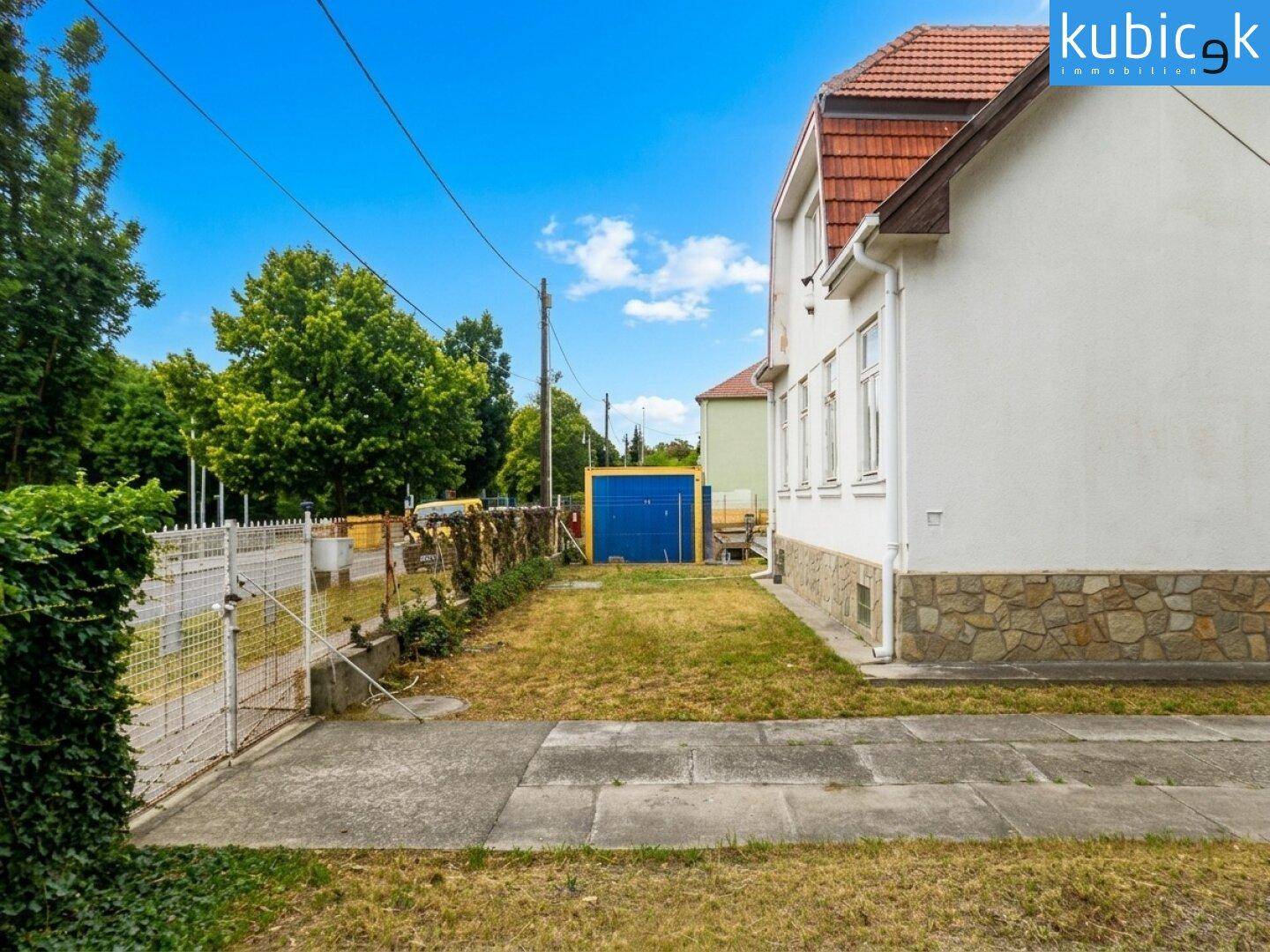 Seitenansicht des Hauses mit Rasenfläche, Zaun und einer blauen Garage im hinteren Bereich.