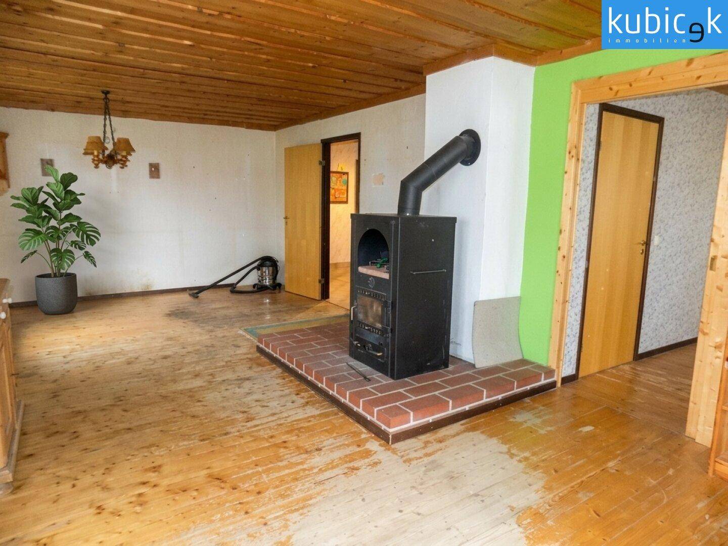 Geräumiges Wohnzimmer mit Holzboden, Holzdecke und einem freistehenden Kaminofen.
