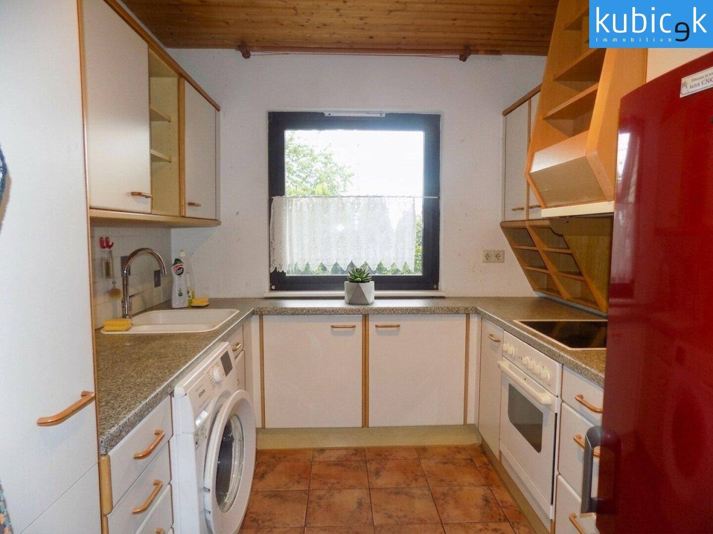 Funktionale Küche mit weißen Schränken, Fliesenboden und Fenster zum Garten.