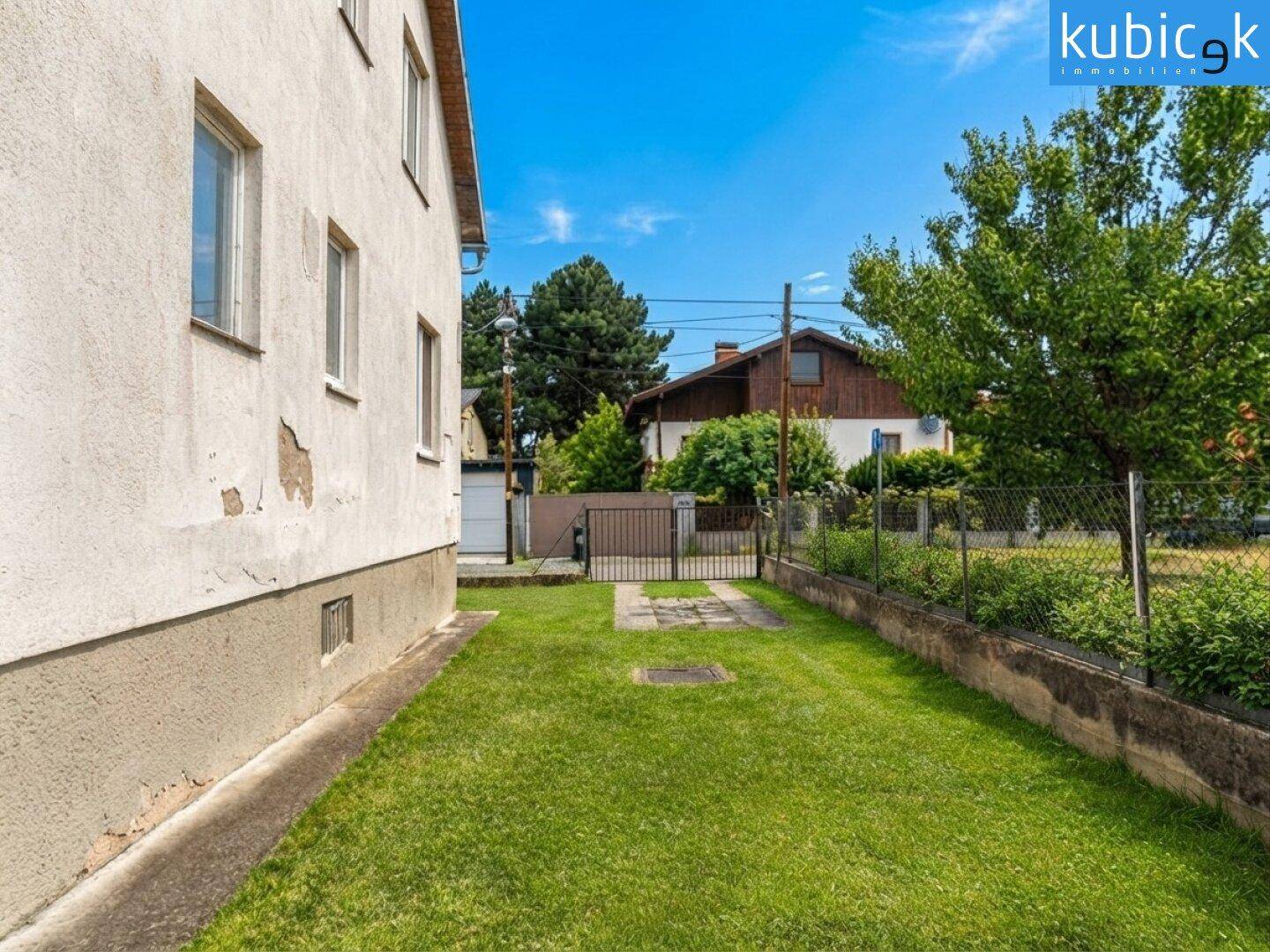 Gepflegter Rasenbereich neben dem Haus mit Blick auf die Nachbarschaft unter blauem Himmel.