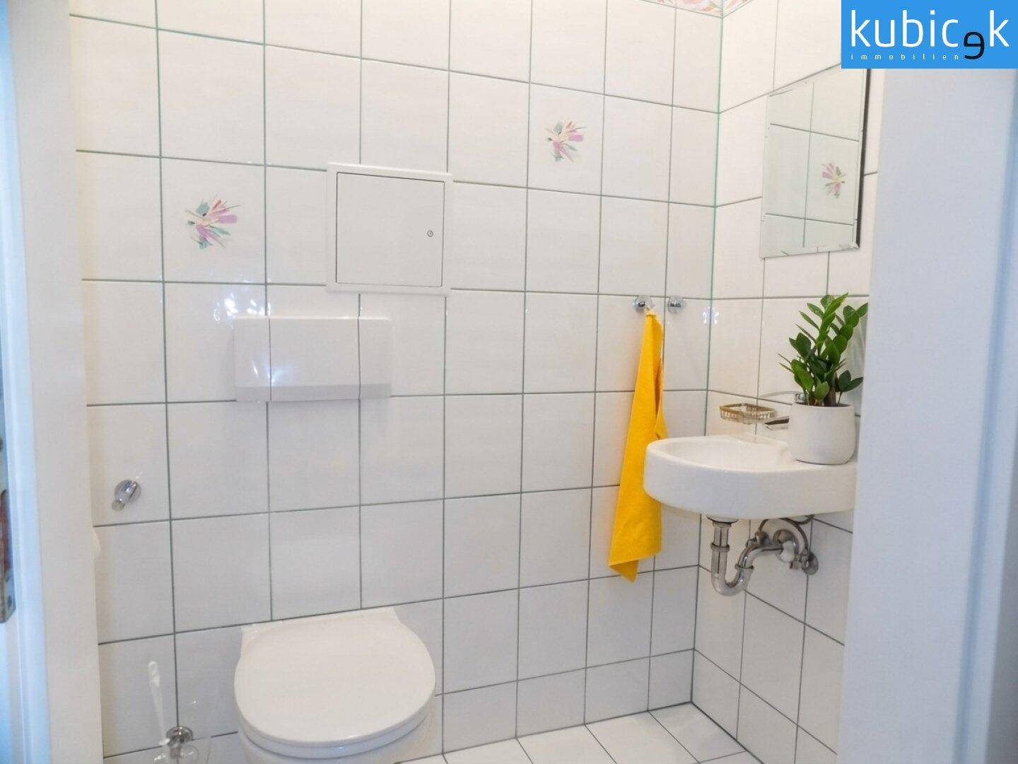 Kleines Gäste-WC mit Toilette, Waschbecken und weißen Wandfliesen.