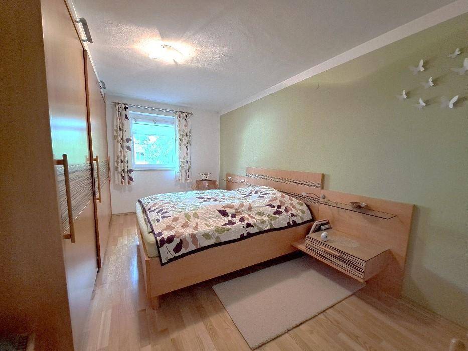 Helles Schlafzimmer mit Holzmöbeln, Parkettboden und Fenster mit Blick ins Grüne.
