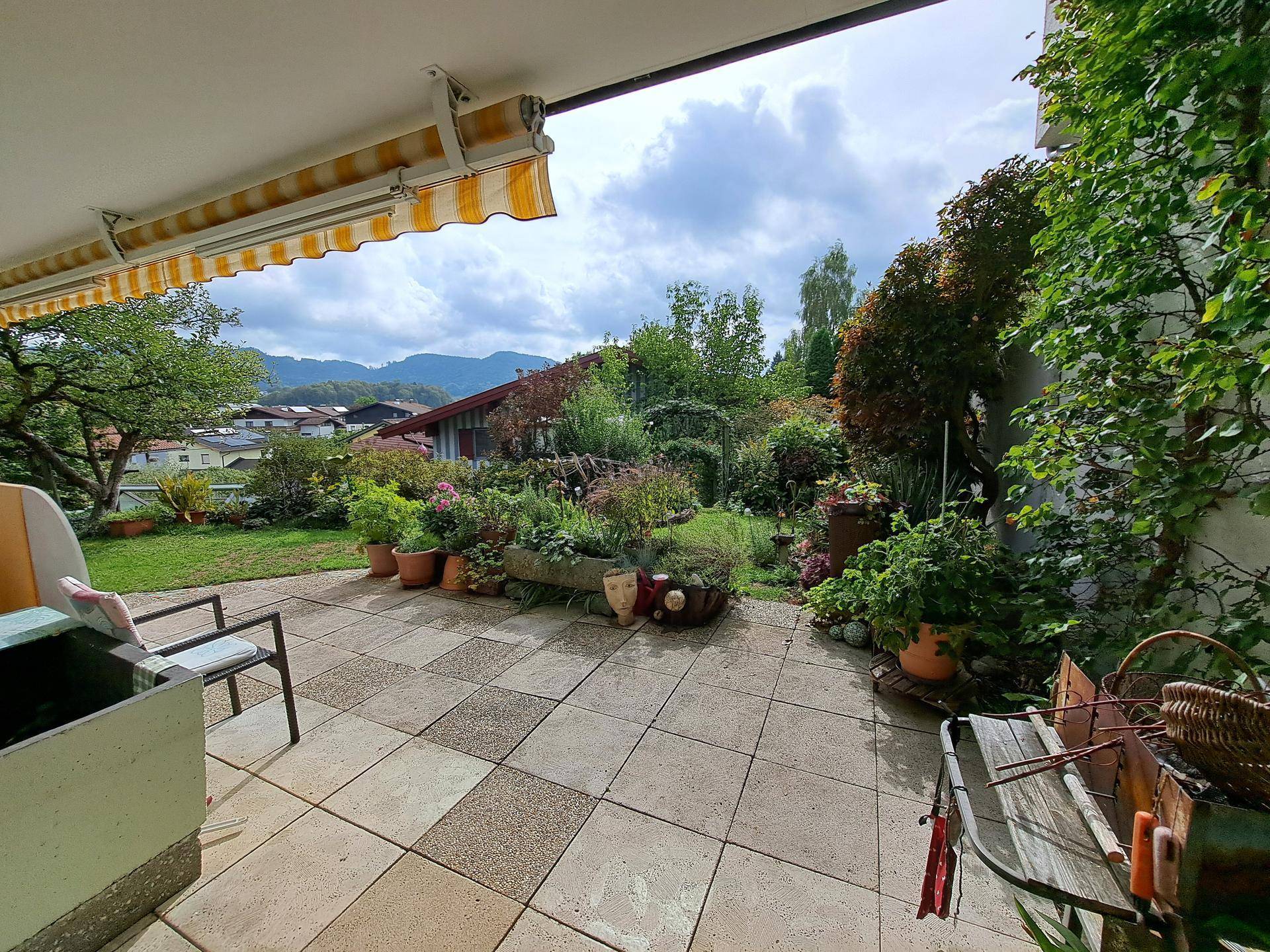 Große gepflasterte Terrasse mit Markise, Gartenmöbeln und weitem Blick auf die Berge.