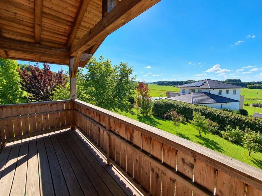 Geräumiger Holzbalkon mit weitem Blick über die grüne Landschaft und Nachbarhäuser.