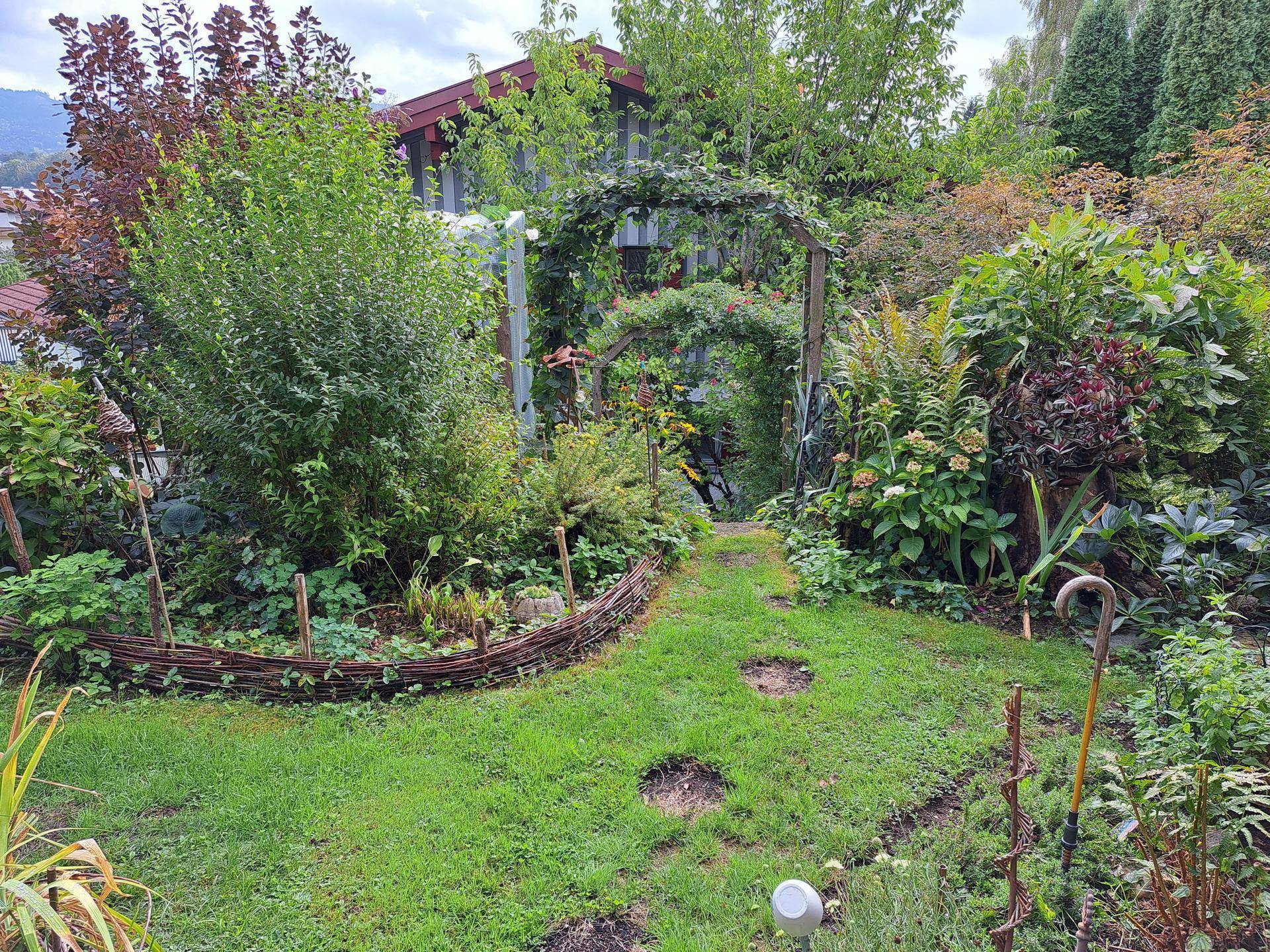 Idyllischer Gartenweg mit üppiger Bepflanzung und einem charmanten Holzbogen.