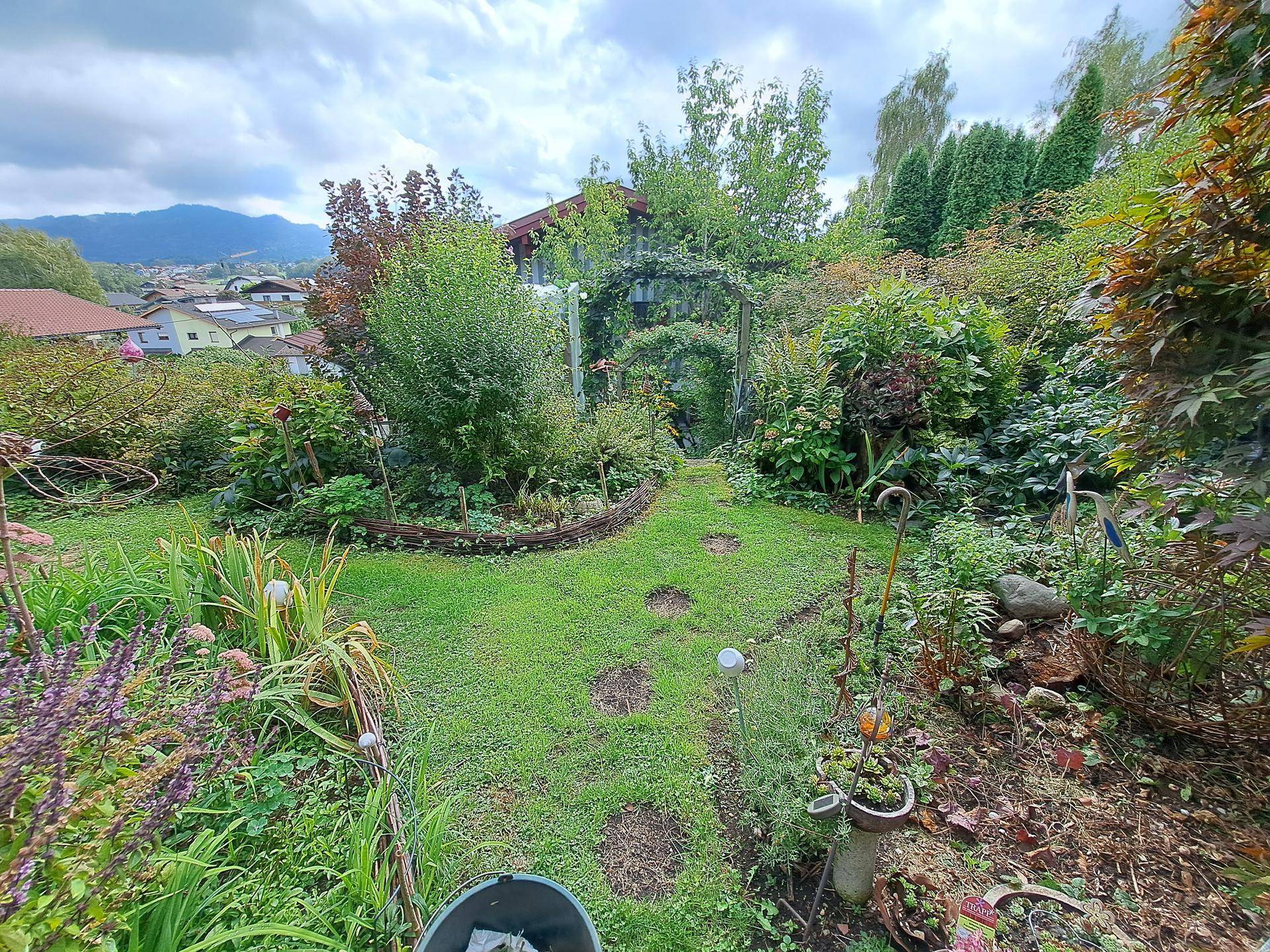 Weitläufiger Garten mit vielfältiger Bepflanzung, Rasen und Blick auf die Berge.