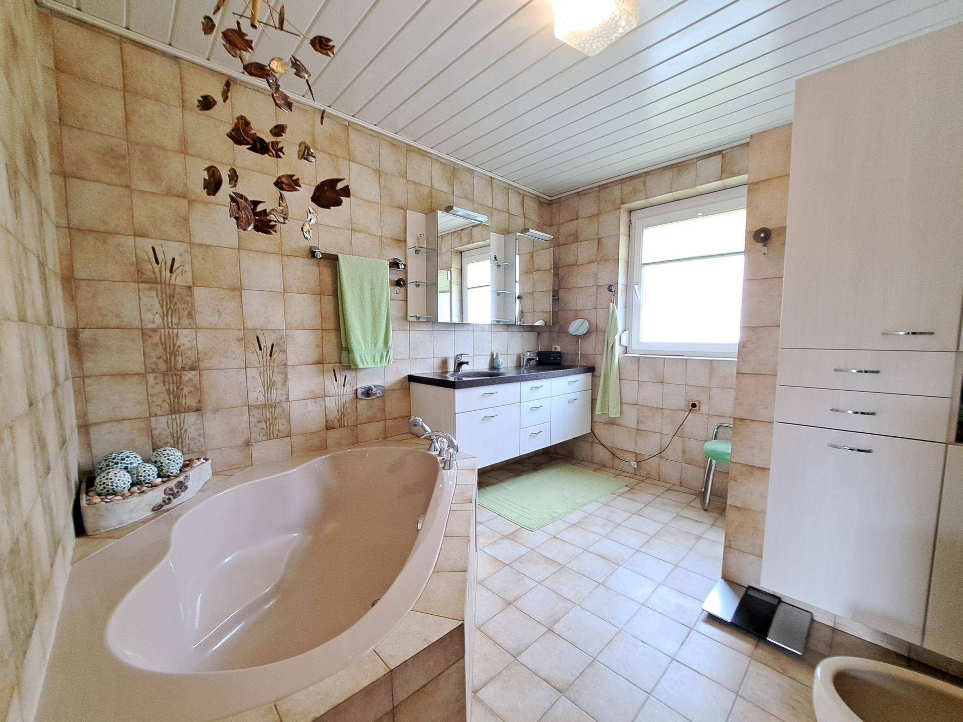 Geräumiges Badezimmer mit Badewanne, Doppelwaschbecken und Fenster.