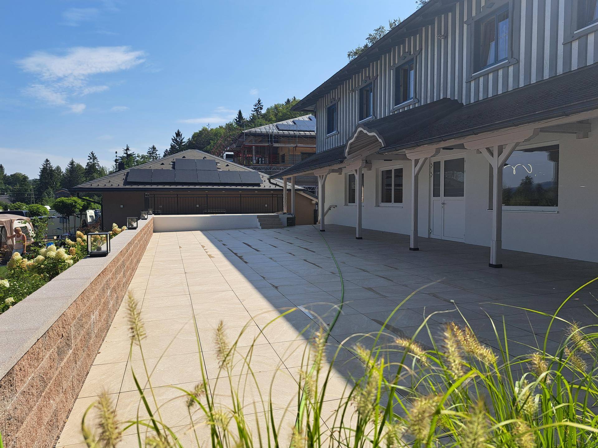 Weitläufige Außenterrasse mit heller Pflasterung, umgeben von einem Gebäude und grüner Landschaft.