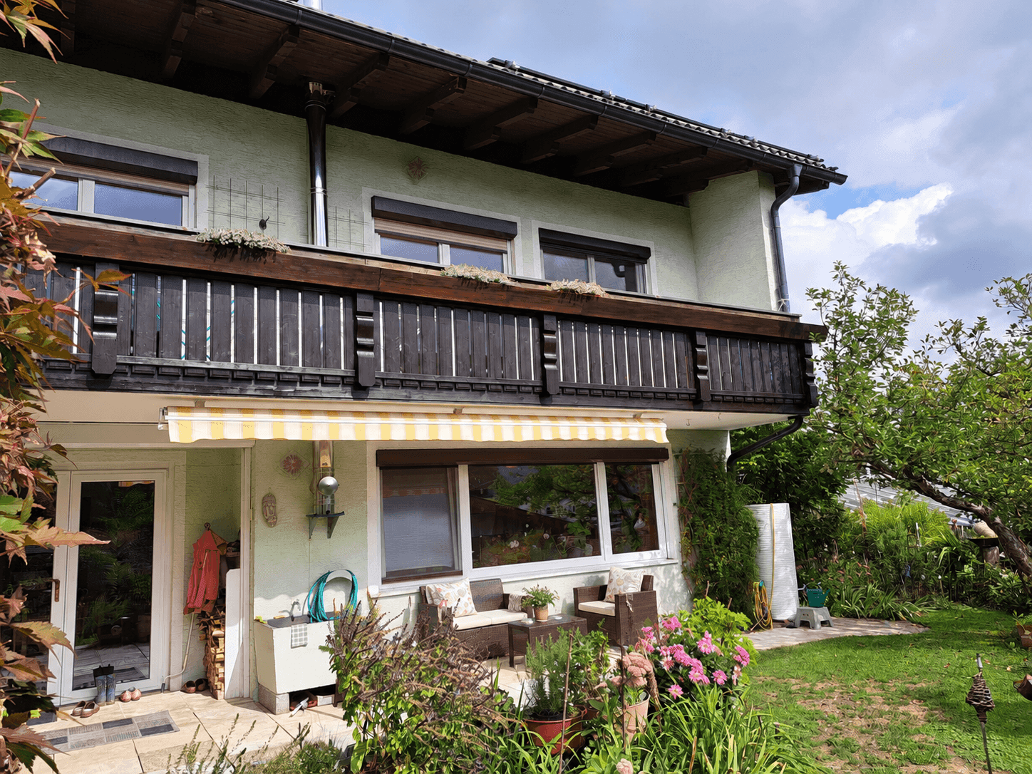 Rückseite des Hauses mit möblierter Terrasse, Balkon und gepflegtem Gartenbereich.