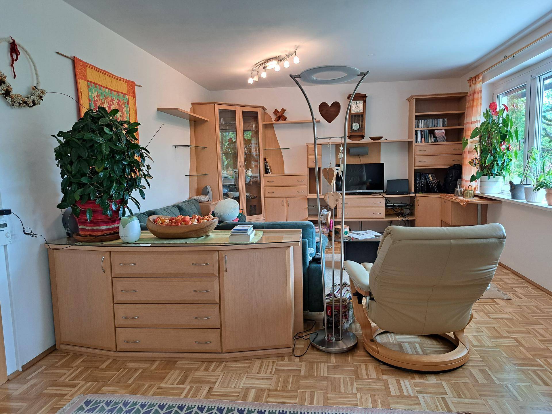 Gemütliches Wohnzimmer mit Parkettboden, Holzmöbeln und viel Tageslicht.