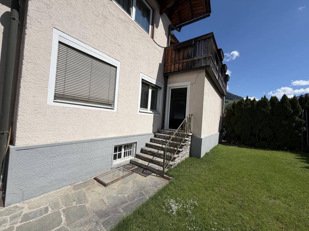 Außenansicht des Gebäudes mit Rasenfläche, Steintreppe und einem kleinen Balkon im oberen Bereich.