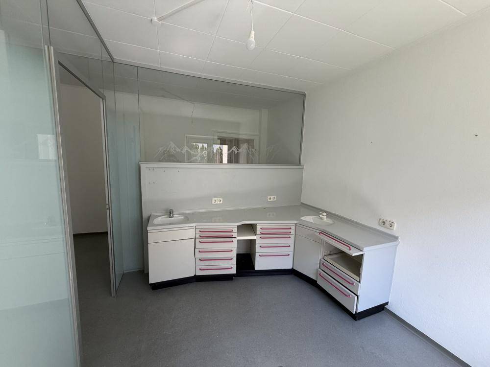 Raum mit grauen Bodenfliesen, Glastrennwand und einem Arbeitsbereich mit zwei Waschbecken.