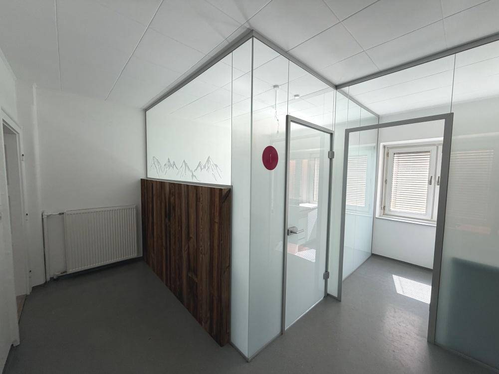 Moderner Büroraum mit Glastrennwänden, Holzakzenten und grauen Bodenfliesen.