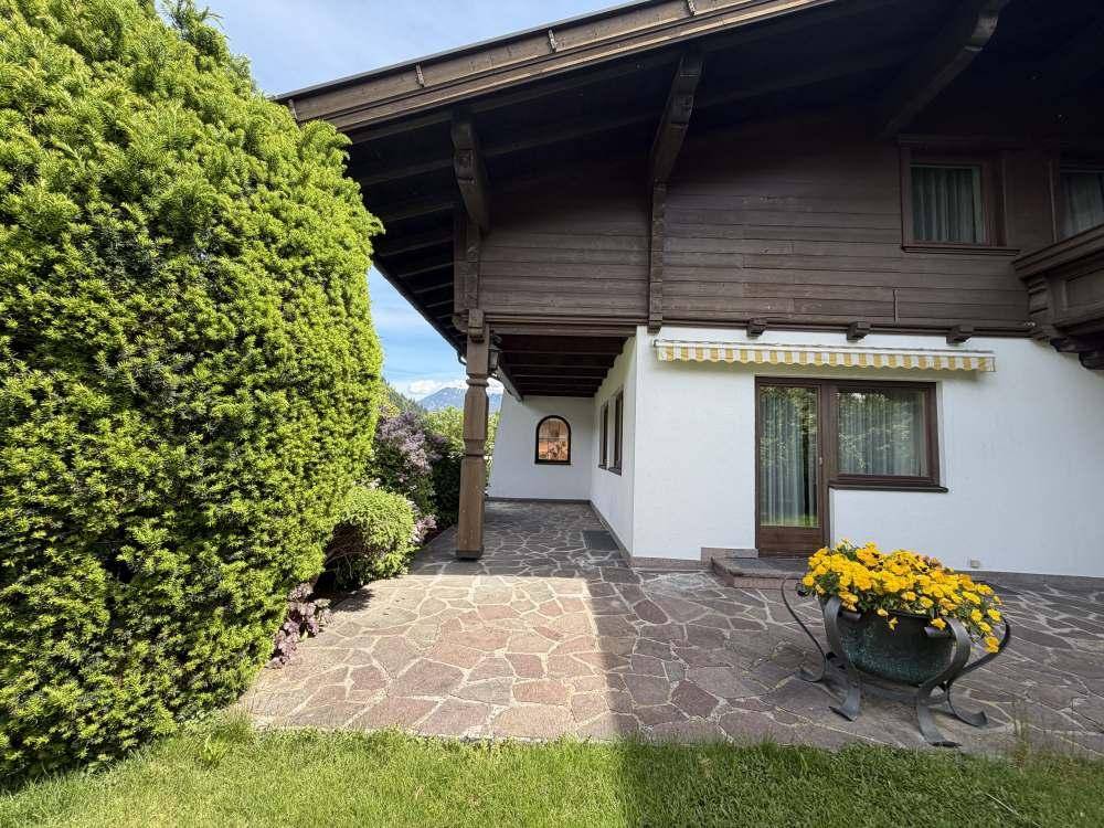 Außenansicht des Hauses mit gepflasterter Terrasse, Rasenfläche und Sträuchern.