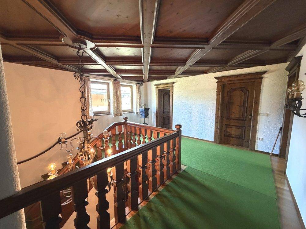 Flur im Obergeschoss mit Holztreppe, sichtbaren Holzbalken und grünem Teppich.