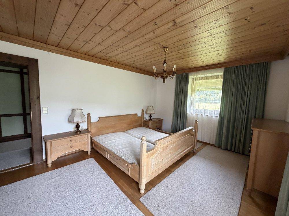 Schlafzimmer mit hellem Holzdoppelbett, Holzdecke und Fenster mit Vorhängen.