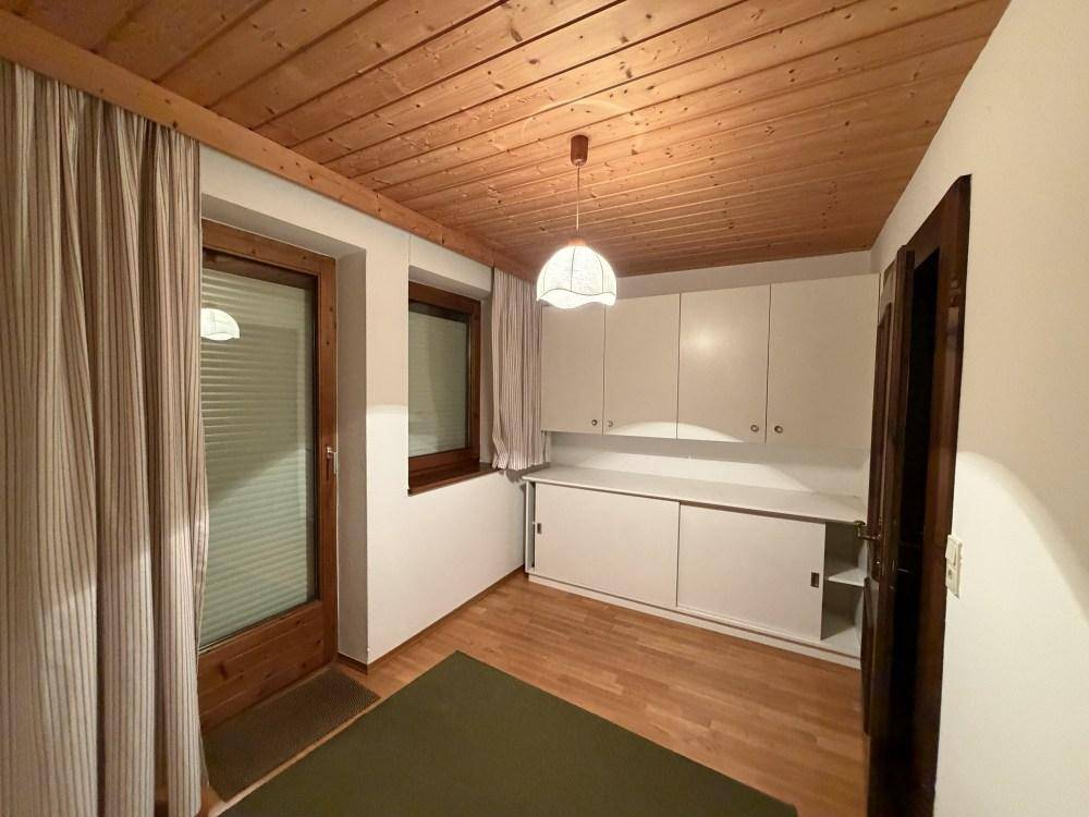 Kleiner Raum mit Holzdecke, weißen Schränken und Zugang zu einem Außenbereich.