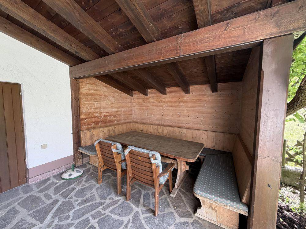 Überdachter Außenbereich mit Holztisch, Bänken und Steinboden.