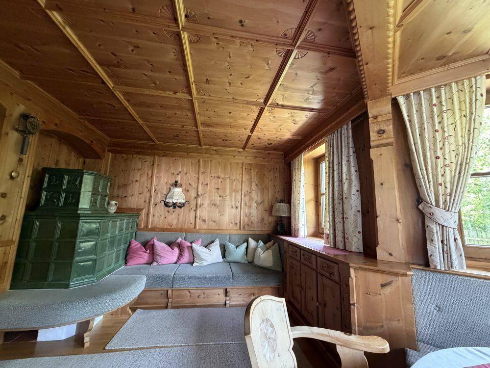 Gemütlicher Wohnbereich im alpinen Stil mit Holztäfelung, Kachelofen und traditionellen Möbeln.