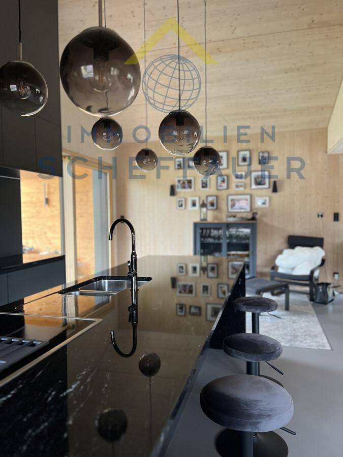 Moderne Küche mit schwarzer Kücheninsel, eleganten Pendelleuchten und offenem Wohnbereich.