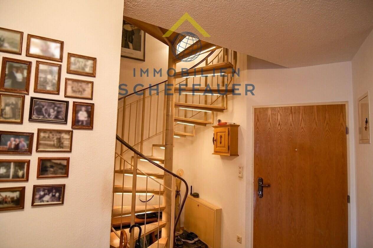Heller Flur mit einer eleganten Wendeltreppe und vielen gerahmten Bildern an der Wand.