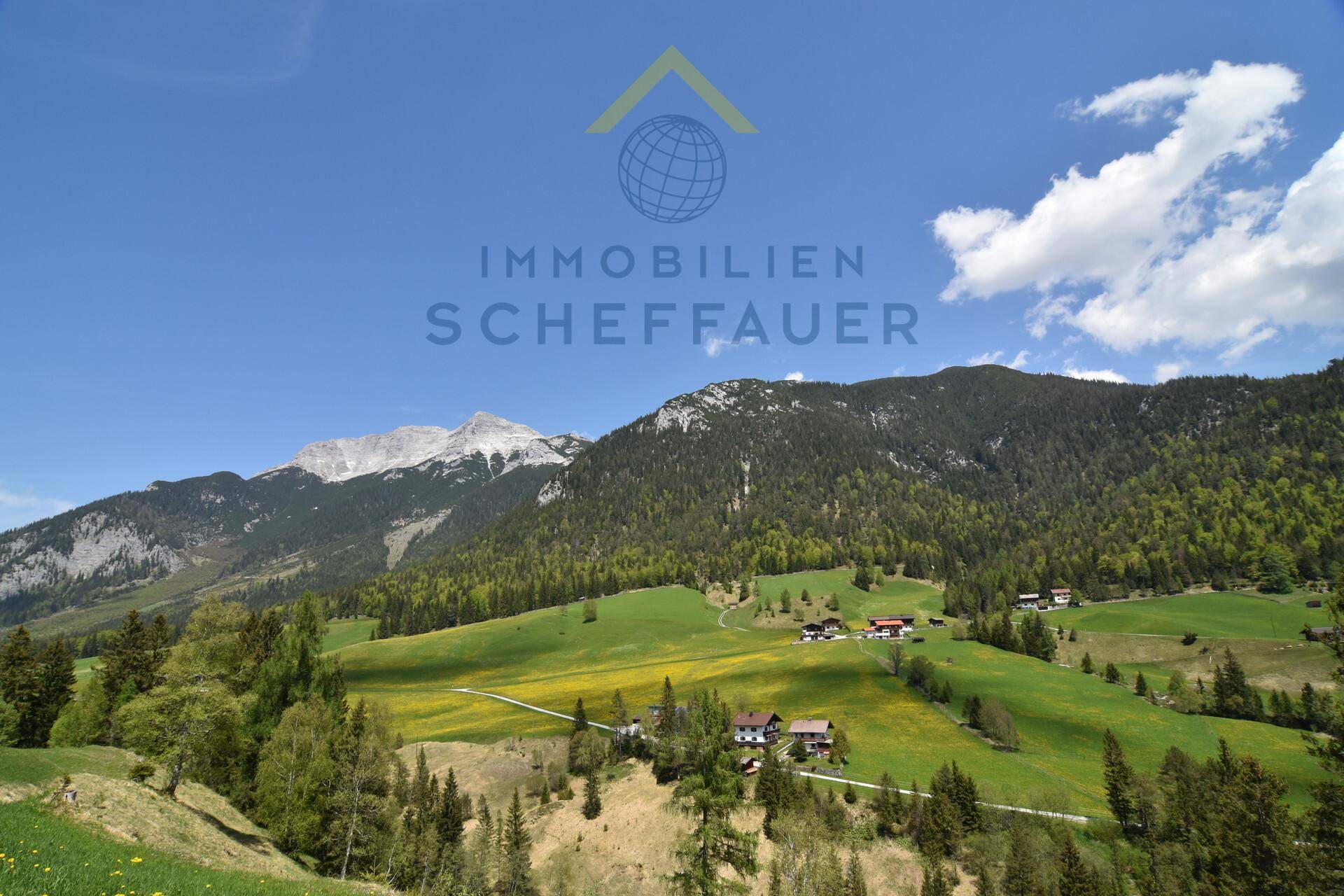 Weitläufige grüne Hügellandschaft mit Bergen und vereinzelten Häusern unter blauem Himmel.