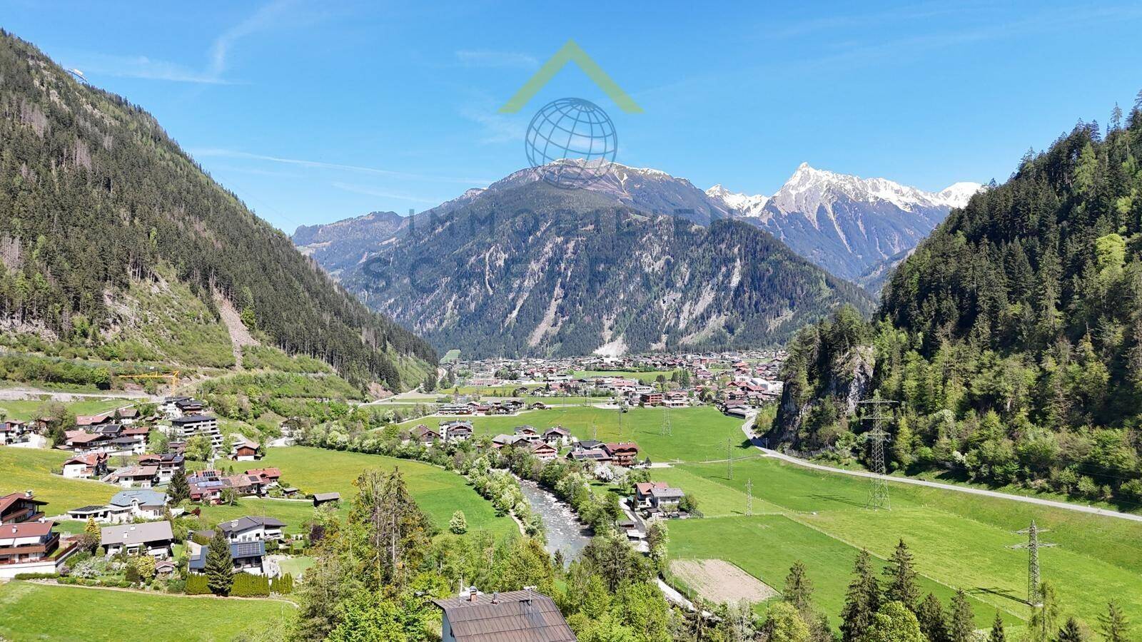 Atemberaubender Weitblick über ein grünes Tal mit einem Dorf und majestätischen Bergen im Hintergrund.