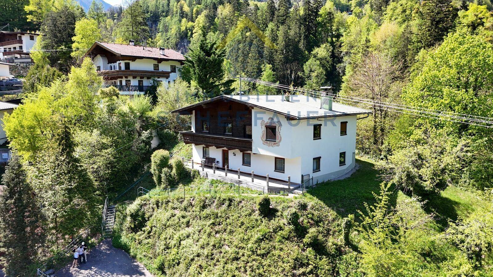 Charmantes Haus in den Bergen, eingebettet in eine grüne Landschaft mit weiteren Gebäuden im Hintergrund.