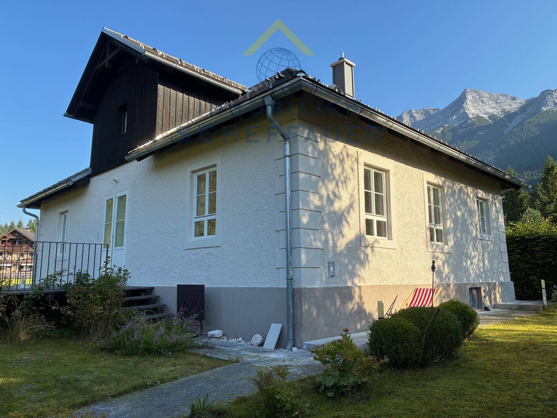Charmantes Haus mit weißer Fassade, Satteldach und Bergblick in grüner Umgebung.