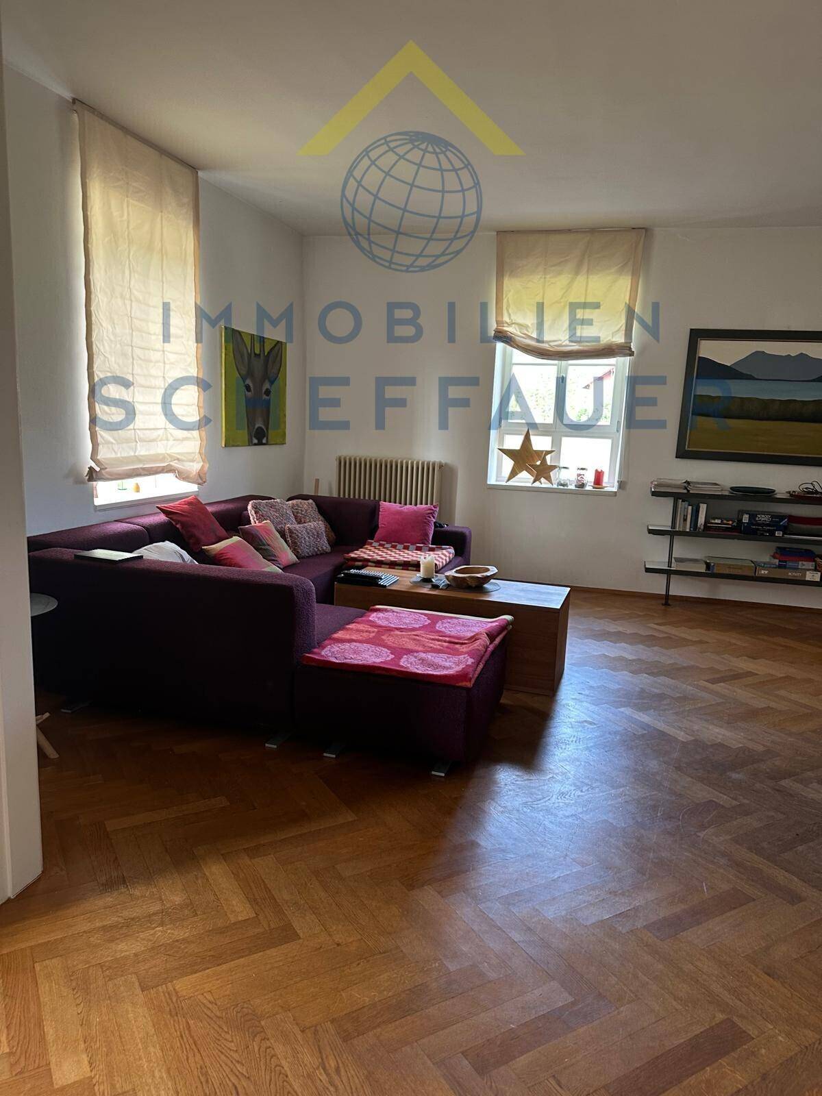 Gemütliches Wohnzimmer mit Parkettboden, großem Sofa und natürlichem Lichteinfall durch Fenster.