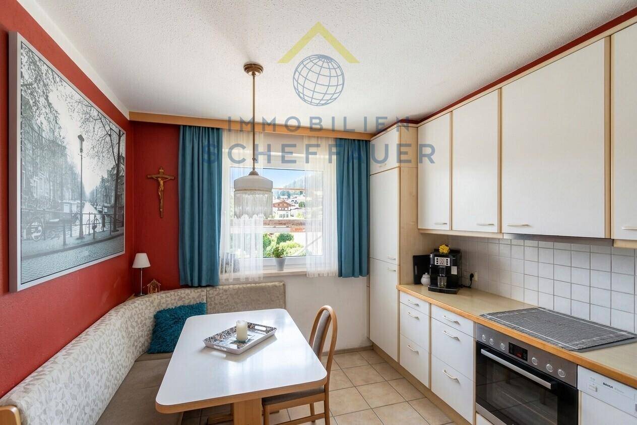 Funktionale Küche mit Essbereich, weißen Schränken, Fliesenboden und Fensterblick.
