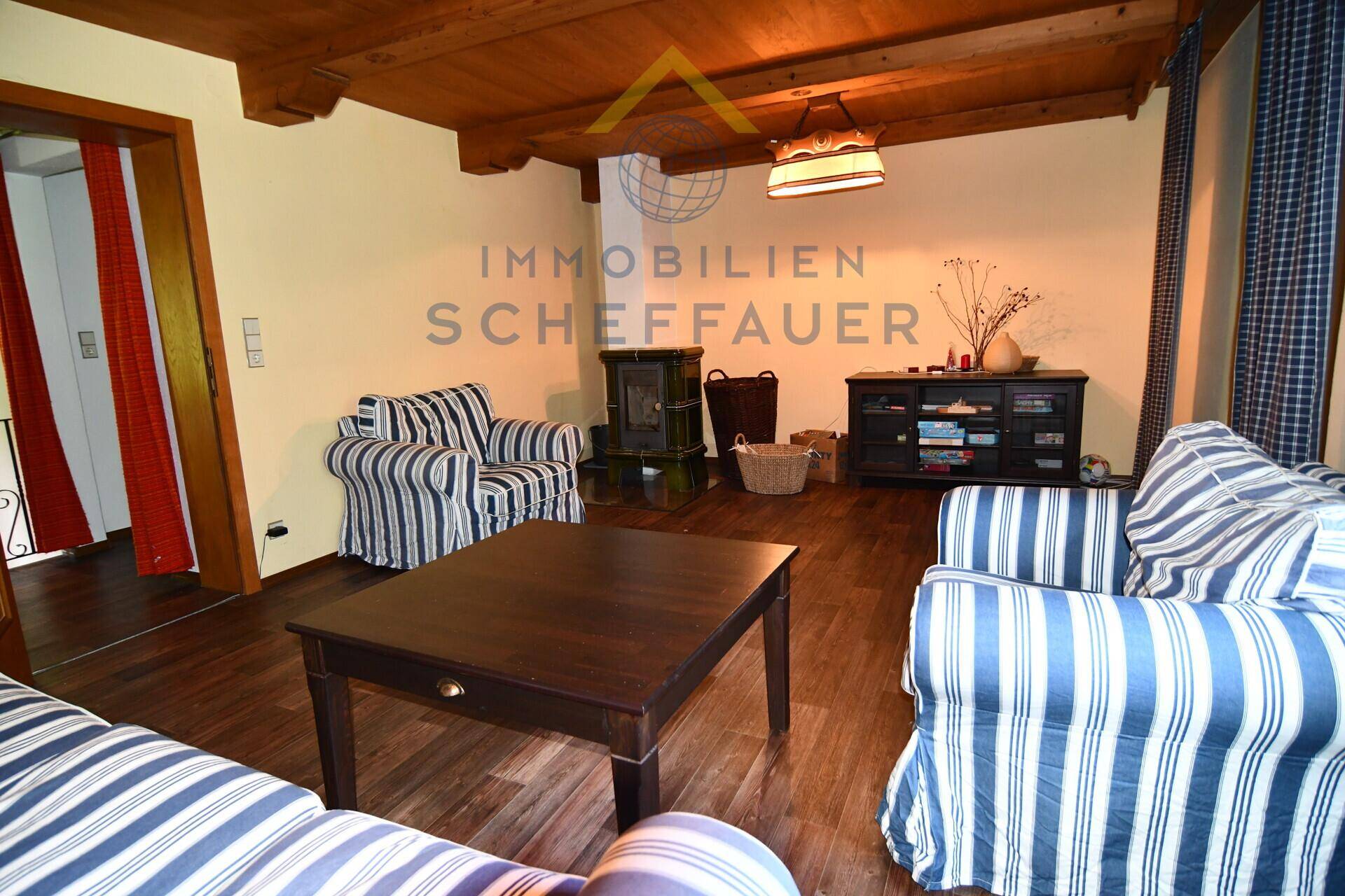 Geräumiges Wohnzimmer mit Holzboden, Holzdecke, gestreiften Sofas und einem Kaminofen.