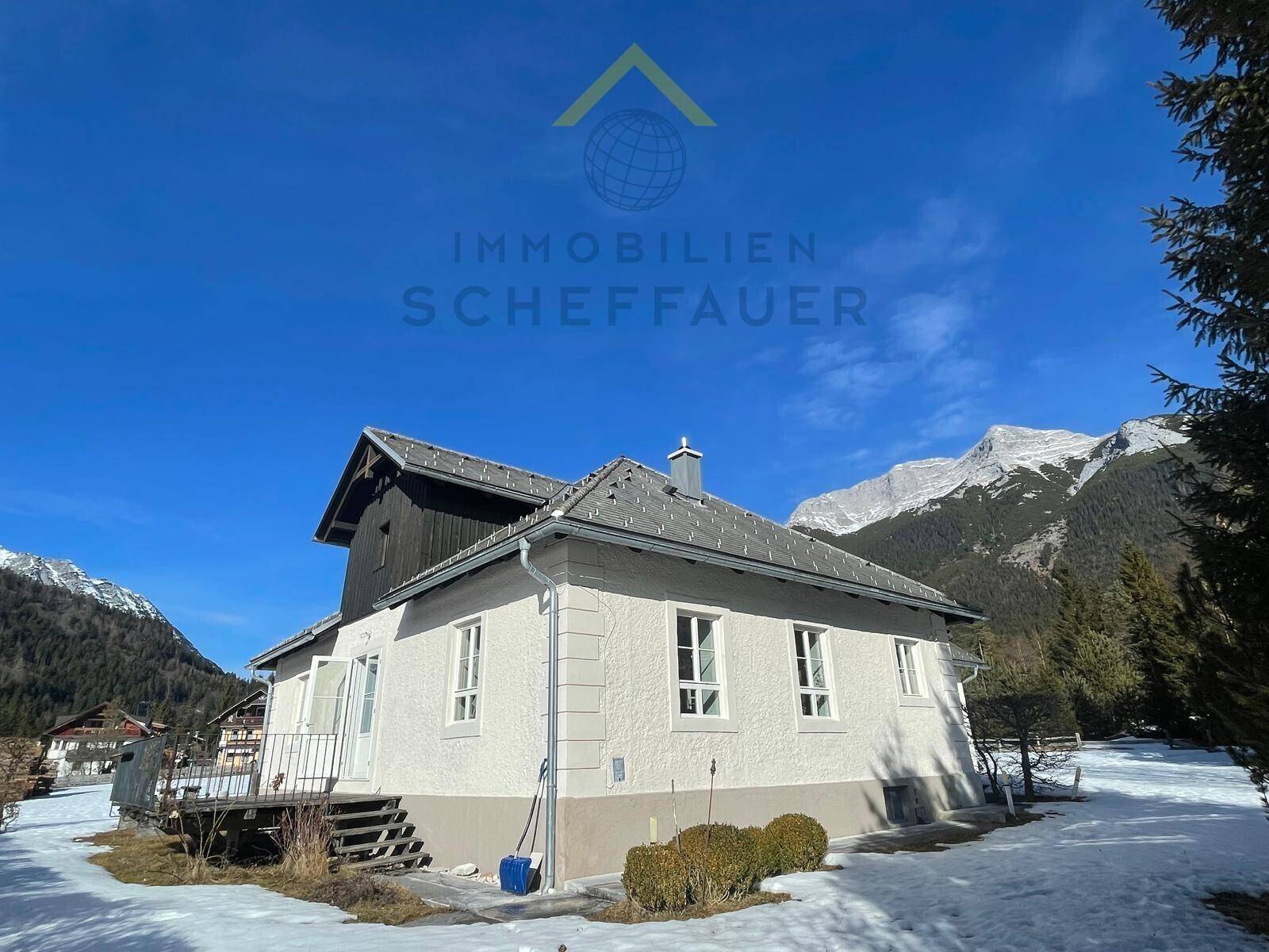 Einfamilienhaus mit weißer Fassade und Satteldach, umgeben von Schnee und Bergen.